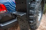 Close-up of a metal utility shelf mounted next to an off-road vehicle's spare tire.