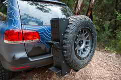 Rear-mounted tire carrier with full-size spare tire on an off-road SUV in a forest setting
