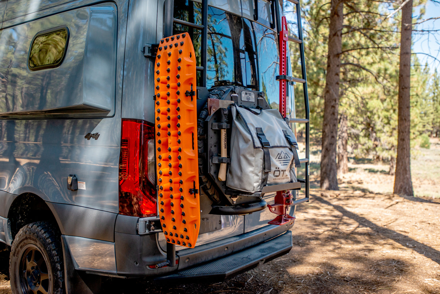 Off-road van with mounted recovery boards and gear bag parked in a forest campsite