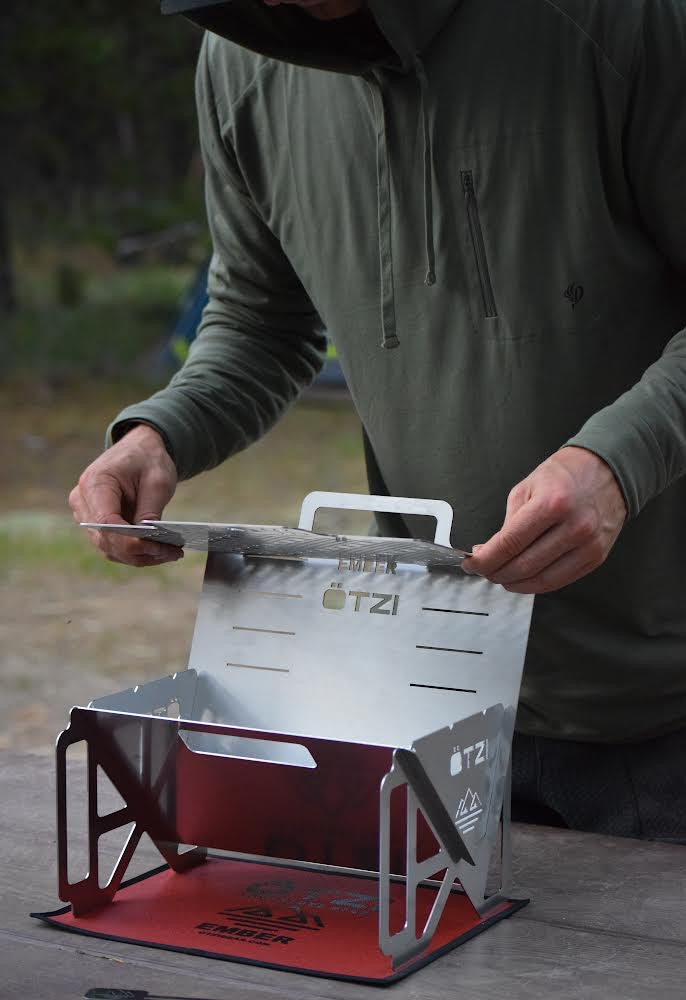 Person assembling a stainless steel portable camping stove on a picnic table.