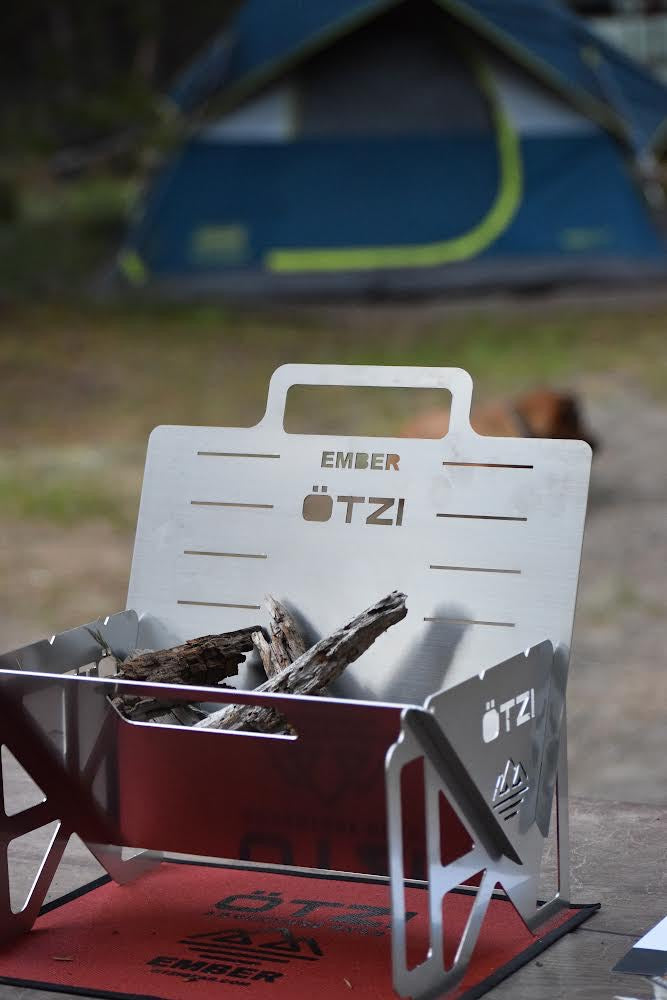 Ötzi Ember portable stainless steel fire pit with firewood, set up at a campsite near a tent