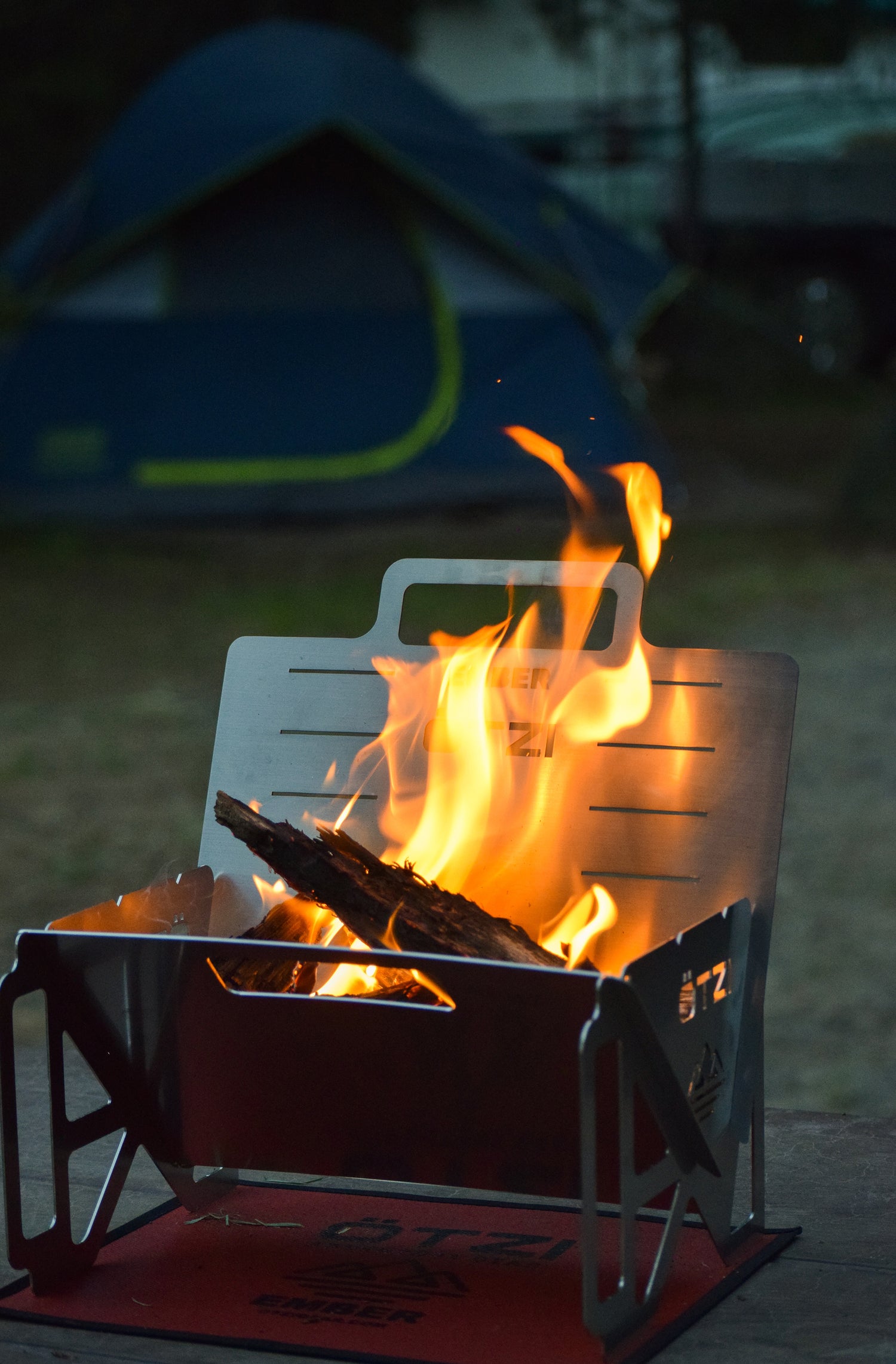 Portable campfire pit with burning wood at a campsite near a blue tent.